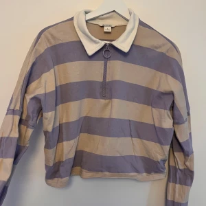 Randig croppad tröja från Monki - Säljer en superfin randig tröja från Monki i storlek S. Den är lila och beige med en cool dragkedja framtill och en vit krage. Perfekt för en avslappnad stil! Tröjan är lite croppad och har långa ärmar. Passar perfekt till både jeans och kjol. 🦄