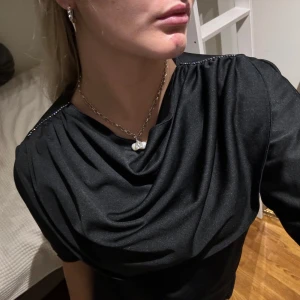 Svart blus med draperad hals - Snygg svart blus med draperad hals och trekvartsärmar. Perfekt för både vardag och fest. Materialet är mjukt och bekvämt, vilket gör den lätt att bära hela dagen. Passar bra med jeans eller kjol för en stilren look.