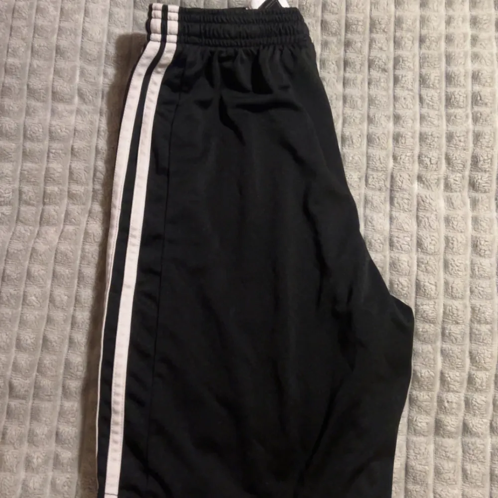 Säljer ett par svarta träningsshorts från Adidas i bra skick. De har en elastisk midja med snörning för perfekt passform. Inga defekter förutom att Adidas-loggan är sprucken.. Sportswear.