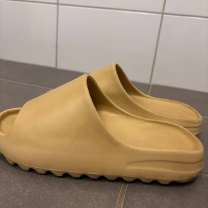 Beige tofflor strl 40 - Säljer ett par bekväma beiga tofflor i syntetmaterial. Perfekta för sommaren med en enkel och stilren design. De har en öppen tå och en tjock sula som ger bra stöd. Passar både till stranden och vardagsbruk.