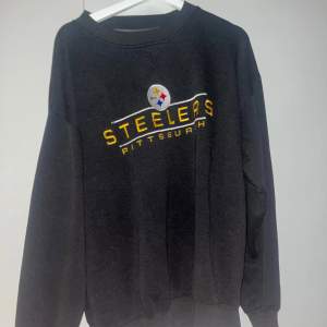 Säljer en svart sweatshirt med Pittsburgh Steelers-logga. Tröjan är i bra skick och har långa ärmar. Perfekt för höst och vinterdagar när du vill hålla dig varm och visa ditt stöd för laget. Passar både till vardags och sportiga tillfällen.