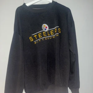 Svart Pittsburgh Steelers sweatshirt - Säljer en svart sweatshirt med Pittsburgh Steelers-logga. Tröjan är i bra skick och har långa ärmar. Perfekt för höst och vinterdagar när du vill hålla dig varm och visa ditt stöd för laget. Passar både till vardags och sportiga tillfällen.