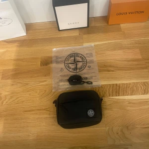 Svart axelväska från Stone Island - Säljer en snygg svart axelväska från Stone Island. Väskan är i nytt skick och har en praktisk dragkedja. Perfekt för vardagsbruk eller när du vill ha en stilren look. Kommer med förpackning och inplastning!