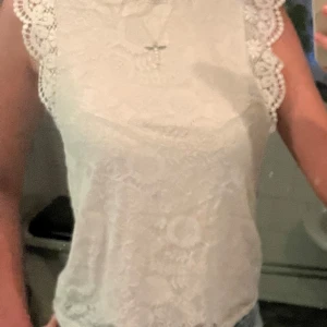 Vit spetsblus - Säljer en superfin vit spetsblus med vackra detaljer. Den är ärmlös och har en elegant spetskant runt ärmhålen. Perfekt för sommarens alla fester eller en stilren vardagslook. Blusen är i mycket bra skick och passar perfekt till både jeans och kjol.
