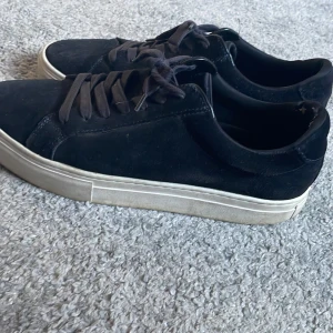 Svarta sneakers från Vagabond - Säljer ett par svarta sneakers från Vagabond i mocka. De har en vit sula och snörning framtill. Skorna är i bra skick men har lite slitage vid hälen. Perfekta för vardagsbruk och passar till det mesta i garderoben. Nypris är 1400. Skick 8,5/10. Pris går o diskutera.