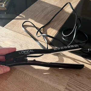 Svart mini plattång från L'Oréal Paris - Säljer en svart plattång från L'Oréal Paris som är bra att ha med på resa. Den är i bra skick och fungerar perfekt. Plattången har en effekt på 35W och är anpassad för 220V. Perfekt för både vardag och fest!
