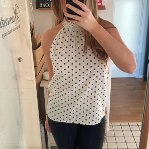 Vit prickig halterneck-topp - Säljer en superfin vit halterneck-topp med svarta prickar. Toppen har en söt spetsdetalj vid halsen och är ärmlös, perfekt för sommardagar. Aldrig använd så i väldigt bra skick ❤️