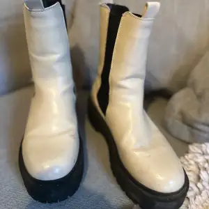 Säljer ett par snygga vita boots i skinn med svarta elastiska paneler på sidorna. De har en rejäl svart sula som ger bra grepp och en cool look. Perfekta för höst och vinter, och de är i storlek dam 37. Använda men i bra skick!