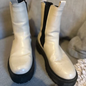 Vita boots med svarta detaljer - Säljer ett par snygga vita boots i skinn med svarta elastiska paneler på sidorna. De har en rejäl svart sula som ger bra grepp och en cool look. Perfekta för höst och vinter, och de är i storlek dam 37. Använda men i bra skick!