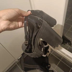 Svarta lackade klackskor - Säljer ett par snygga svarta lackade klackskor med rem. De har en rejäl klack och en stilren design som passar perfekt för festliga tillfällen. Skorna är i bra skick och har en justerbar rem för bästa passform. Storlek 39 