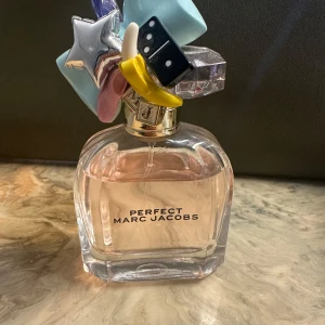 Perfect Marc Jacobs parfym - Säljer en superfin parfym från Marc Jacobs, 'Perfect'. Flaskan är 50 ml och har en unik design med en massa färgglada detaljer på korken, som en stjärna och en tärning. Perfekt för dig som älskar en söt och fräsch doft! Flaskan är nästan full och i bra skick. Passa på att köpa denna lyxiga doft! 🌟