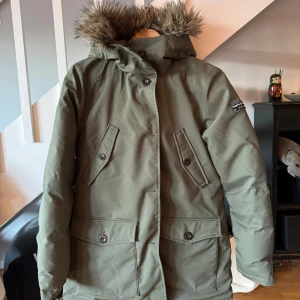 Grön vinterjacka från Peak Performance - Säljer en grön vinterjacka från Peak Performance i mycket bra skick. Jackan har en mysig pälskantad huva och är fodrad med blått foder. Perfekt för kalla vinterdagar! 🧥❄️