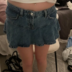 Jeanskjol med volang - Säljer en superfin jeanskjol med volangdetaljer. Den är kort och perfekt för sommaren. Har inbyggda shorts Kjolen har en klassisk blå jeansfärg och är i bra skick. Passar perfekt till en avslappnad dag eller en somrig fest!