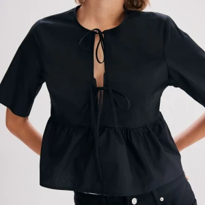 Svart blus med knytning - Snygg svart blus med knytning framtill. Köpt för 199kr. Den har korta ärmar och en lös passform som ger en avslappnad look. Perfekt för både vardag och festliga tillfällen. Tillverkad i ett lätt och bekvämt material.