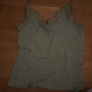 Grön ribbad linnetopp från Amisu - Säljer en söt grön ribbad linnetopp från Amisu i storlek XXS. Toppen har spetsdetaljer vid halsringningen och smala axelband. Perfekt för sommardagar eller som ett lager under en kofta. Använd men i bra skick.