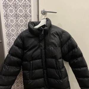 Svart dunjacka från Helly Hansen - Säljer en svart dunjacka från Helly Hansen i mycket bra skick, knappt använd. Väldigt fin jacka som är i barnstorlek 164 men lite större i storleken. Tyvärr saknas luvan💕