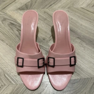 Rosa klackskor med spänne - Säljer ett par snygga rosa klackskor. De har en stilren design med två spännen på ovansidan och en elegant spetsig tå. Perfekta för sommarens fester eller en utekväll. Skorna är i mycket bra skick och redo att användas!