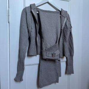 Grå stickad hoodie och byxor set - Säljer ett supermysigt grått set med stickad hoodie och matchande byxor. Hoodien har dragkedja och långa ärmar, perfekt för kyliga dagar. Byxorna är bekväma med ribbade detaljer och ett bälte i midjan. Perfekt för en avslappnad stil hemma eller ute.