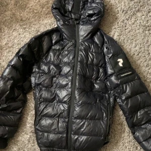 Svart dunjacka med huva - Säljer en snygg svart dunjacka med huva, perfekt för kalla dagar. Jackan har en stilren design med dragkedja framtill och är i mycket bra skick. Den är varm och bekväm, idealisk för både höst och vinter. Passar perfekt för dig som vill hålla stilen även när det är kallt ute!