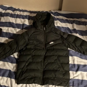 Svart pufferjacka från Nike - Säljer en svart pufferjacka från Nike i ganska bra skick. Nypris 1200, Jackan har en dragkedja framtill och en huva för extra värme. Perfekt för kalla höst- och vinterdagar. Den är långärmad och har en stilren design med Nike-loggan på bröstet. Passar både till vardags och sportiga aktiviteter.