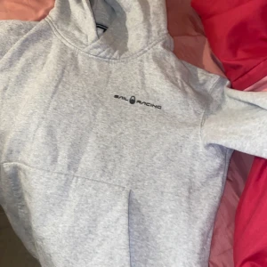 Grå hoodie från Sail Racing - Säljer en snygg och bekväm grå hoodie från Sail Racing. Den har en klassisk känguruficka och en justerbar huva. Perfekt för kyliga dagar eller som ett stilrent vardagsplagg. Passar både till jeans och träningsbyxor! Använd Max 2 gånger och säljer på grund av att den är för stor för mig