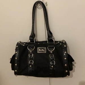 Svart axelväska med nitar - Snygg svart axelväska med coola nitar och detaljer i syntetmaterial. Väskan har en rektangulär form och är perfekt för en rockig stil. Den har dubbla handtag och en praktisk dragkedja upptill. Perfekt för både vardag och fest! Pris går att diskuteras!