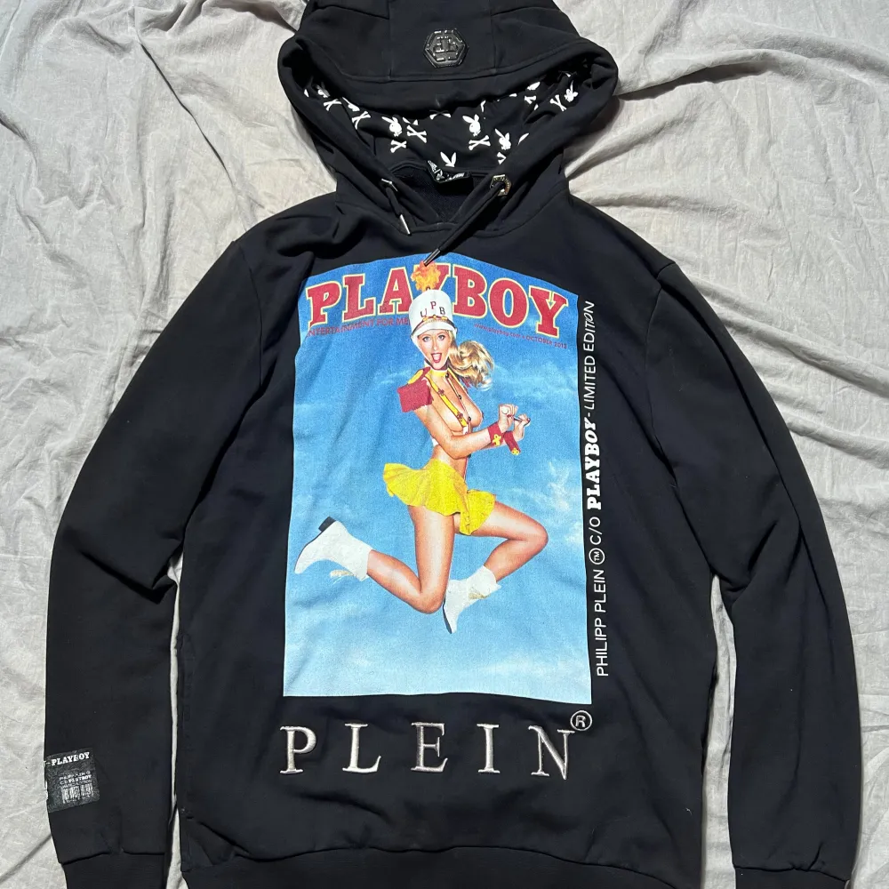 Säljer en svart hoodie från Philipp Plein i samarbete med Playboy. Den har en stor färgglad tryck på framsidan och text på baksidan. Insidan av huvan är mönstrad, med PP loggan på huvan i metall. Perfekt för en cool och avslappnad stil! Köptes hos plein.com för något år sen för 6800kr, säljes för 600kr. Snygg och väl omhändertagen hoodie, använd extremt sällan. Storleken är XL, sitter litet, passar mig som är 180cm och har storlek L. . Hoodies.