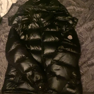 Svart pufferjacka från Moncler - Säljer en snygg svart pufferjacka från Moncler i mycket bra skick. Jackan har en glansig finish och är perfekt för kalla dagar. Den har en dragkedja framtill och långa ärmar. Insidan har ett coolt serietidningsmönster. Perfekt för vintern! ❄️ (pris går att diskutera) 