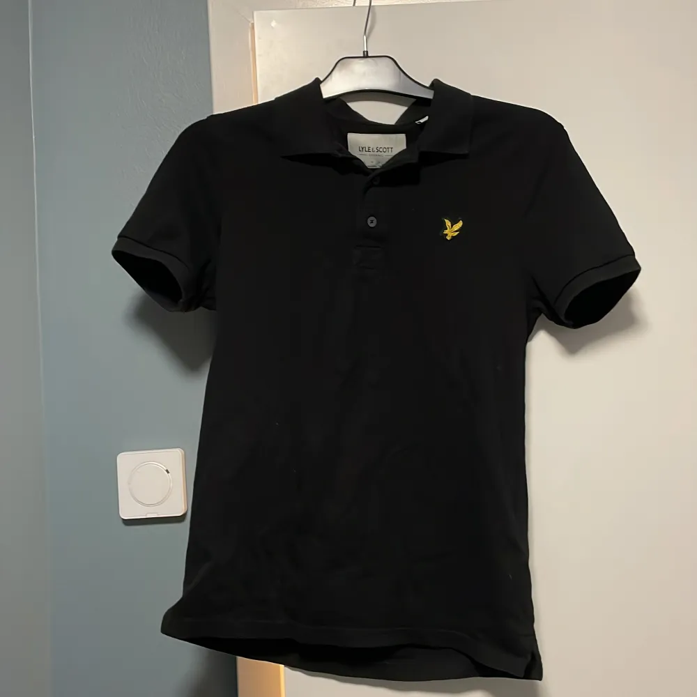Säljer en snygg svart pikétröja från Lyle & Scott i storlek S. Tröjan är i bra skick och har en klassisk design med korta ärmar och en liten broderad logga på bröstet. Perfekt för både vardag och fest! . T-paidat.