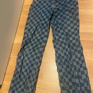 Rutig denimbyxa med hög midja - Säljer ett par coola rutiga denimbyxor med hög midja och wide leg. Perfekta för en avslappnad stil med en twist. Byxorna är i bra skick och har en unik design som sticker ut. Passar perfekt för både vardag och fest!