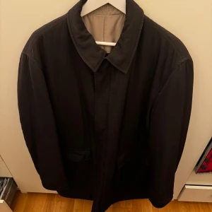 Kappa från Pal Zileri - Säljer en elegant tvåsidig svart/beige kappa från Pal Zileri Concept. Rocken har en klassisk design med krage och dolda knappar framtill. Perfekt för höst och vinter, och ger en stilren look. Den är i mycket bra skick och passar både till vardags och mer formella tillfällen.