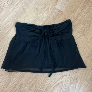 Svart topp med snörning - Snygg svart topp med snörning framtill. Perfekt för både vardag och fest! Toppen har en enkel design med en liten volangdetalj som ger den en extra touch. Materialet känns mjukt och bekvämt, vilket gör den idealisk för sommaren.