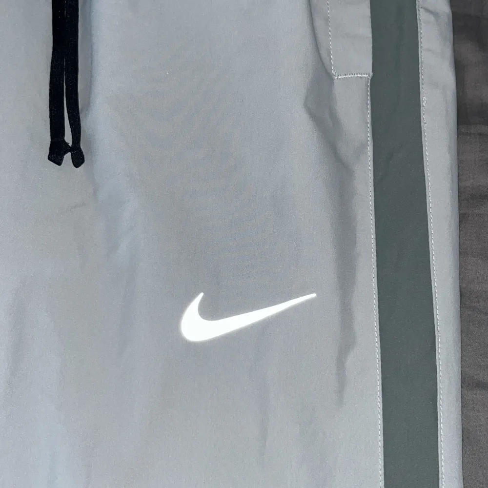 Säljer ett par grå träningsbyxor från Nike i Dri-FIT material. De har en elastisk midja med snörning och en reflekterande Nike-logga på benet. Perfekta för träning eller en avslappnad dag. 🏃‍♂️ dom är som helt nya inte ens använda en gång. Jeans & Byxor.