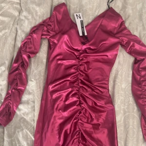 Rosa klänning från Boohoo - Säljer en superfin rosa klänning  i ett glansigt material. Den har långa ärmar och en snygg rynkad detalj baktill som ger en smickrande passform. Perfekt för festliga tillfällen! 💖I affären såldes den för 450 kr men jag säljer den för 370kr samt det går att pruta.