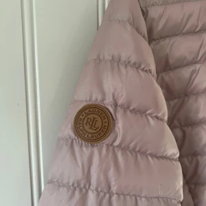 Rosa lättvikts dunjacka från Ralph Lauren - Säljer en superfin rosa dunjacka från Ralph Lauren i storlek M. Jackan har en dragkedja framtill och en snygg quiltad design. Perfekt för höst och vår när det är lite kyligt ute. Den är i mycket bra skick och har en stilren look som passar till det mesta. 🌸