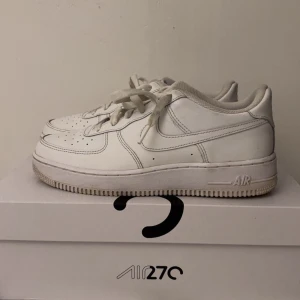 Vita Nike Air Force sneakers - Säljer ett par klassiska vita Nike Air Force sneakers i bra skick. De har en stilren design med snörning och perforerade detaljer för ventilation. Perfekta för vardagsbruk och passar till nästan alla outfits. Skorna är bekväma och har en stadig sula.
