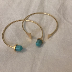 Guldarmband med turkosa stenar - Två stilrena guldarmband med en unik design. Ena änden har en turkos sten och den andra en guldig triangel. Perfekta för att ge en färgklick till din outfit. Passar både till vardag och fest!💗