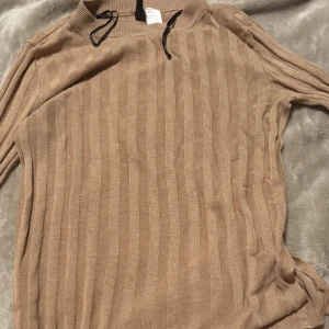Beige stickad tröja med slit - Säljer en mysig beige stickad tröja med slit och randigt mönster. Perfekt för höst och vinter. Tröjan har långa ärmar och en avslappnad passform. Perfekt för att hålla sig varm och stilren under kyliga dagar.