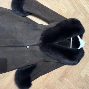 AMORESS Betty merinolammskappa med päls i blåräv - Säljer min eleganta bruna mockakappa med lyxiga svarta pälsdetaljer på krage och ärmslut. Ordpris: 28 000kr                                                   Mitt pris:4000kr          Kan mötas upp eller frakta.  först till kvarn!