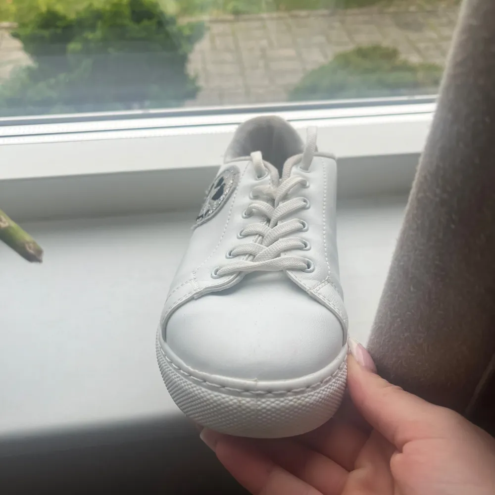 Snygga vita sneakers från SmileyWorld med en glittrig smiley på sidan. Skorna har snörning och en bekväm passform. Köpta för ett år sen men knappt använda. De är i mycket bra skick och redo för ny ägare. Storlek 37. Skor.