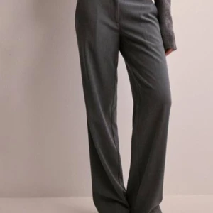 Grå kostymbyxor - Säljer ett par stilrena grå kostymbyxor i mycket bra skick. De har en klassisk design med låg midja och en rak passform som ger en elegant look. Perfekta för både kontoret och mer formella tillfällen. Materialet känns mjukt och bekvämt mot huden.