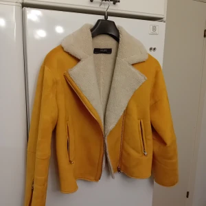 Gul jacka med foder från Zara - Säljer en snygg gul jacka från Zara med mysigt vitt foder. Jackan har dragkedja och långa ärmar, perfekt för höst och vinter. Den är i mycket bra skick och passar både till vardags och fest. Storlek dam M.