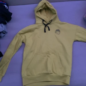Gul hoodie från Burton - Säljer en snygg gul hoodie från Burton i bra skick. Den har en klassisk känguruficka och en justerbar huva med svarta snören. Perfekt för höst och vår när du vill vara både bekväm och stilren. Passar till både chill och vardagsäventyr!