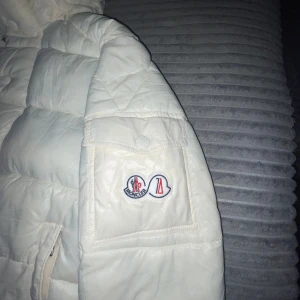 Vit Moncler jacka  - Säljer en moncler vit jacka i mycket bra skick. Jackan har en quiltad design med en huva och knappar framtill. Perfekt för kalla vinterdagar.