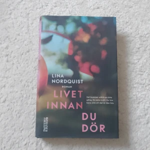 Livet innan du dör - Romanen 'Livet innan du dör' av Lina Nordquist är en gripande berättelse om fyra grannar i Uppsala. Boken utforskar teman som kärlek, livets skörhet och oväntade händelser. Omslaget har en suddig bild med varma färger som ger en känsla av mystik och djup.
