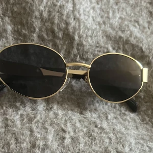 Ovala solglasögon med gulddetaljer - Snygga ovala solglasögon med guldfärgad ram och svarta glas. Aldrig använda