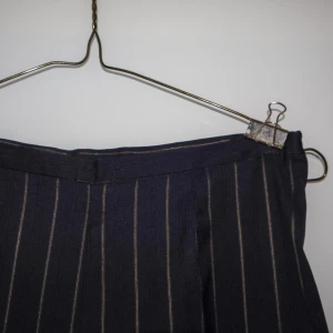 Marinblå randiga kostymbyxor - Snygga marinblå kostymbyxor med tunna vita/guldiga ränder. Perfekta för både kontoret och festliga tillfällen. Byxorna har en klassisk passform och är tillverkade i ett bekvämt material som ger en stilren look. Ett måste i garderoben för den som vill ha en tidlös stil!