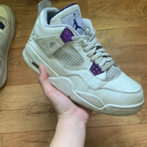 Purple methalic J4 - Säljer ett par snygga Nike Air Jordans i vitt med lila detaljer. Skorna har en klassisk design med snörning och är i bra skick. Perfekta för både vardag och fest! 🏀