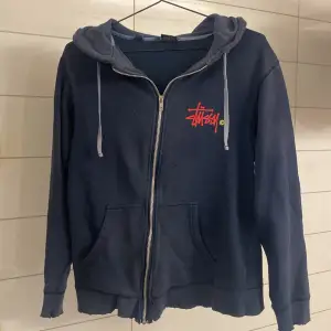 Säljer en mycket sällsynt mörkblå hoodie från Stüssy med dragkedja och huva. Den har en cool logga på framsidan och grön på baksidan. Perfekt för en avslappnad stil. Lite slitage på muddarna, men annars i bra skick. Perfekt för kallare väder! Storlek M men passar som S/Xs. Skriv vid minsta funderingar!