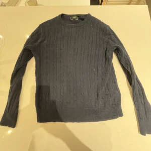 Mörkblå stickad tröja från Boomerang - Säljer en snygg mörkblå stickad tröja från Boomerang. Perfekt för kyliga dagar med sitt klassiska mönster och ribbade kanter. Tröjan har långa ärmar och en rund halsringning. Passar både till vardags och lite finare tillfällen. 🧶